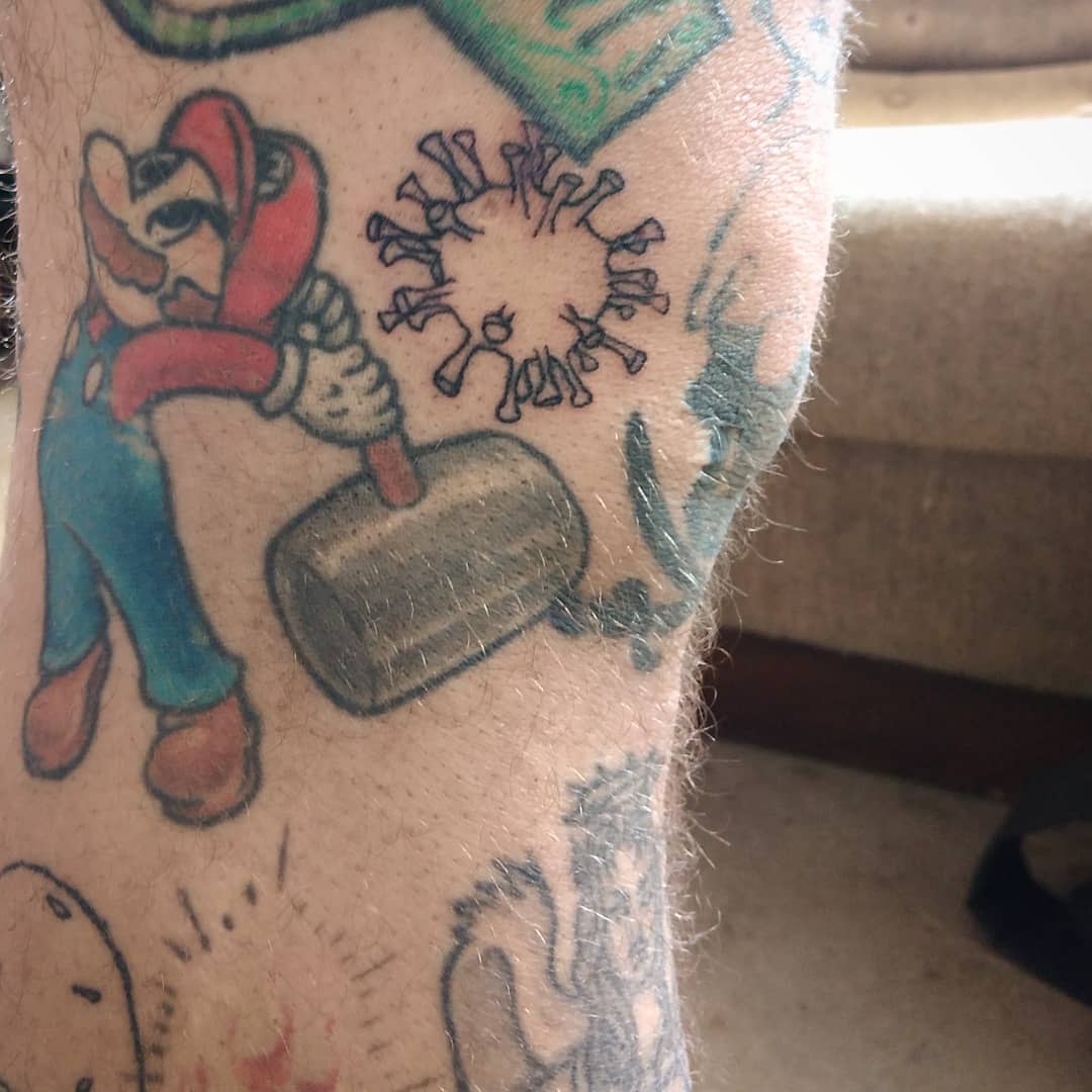 Tattoo of a character holding a hammer next to a virus on a leg