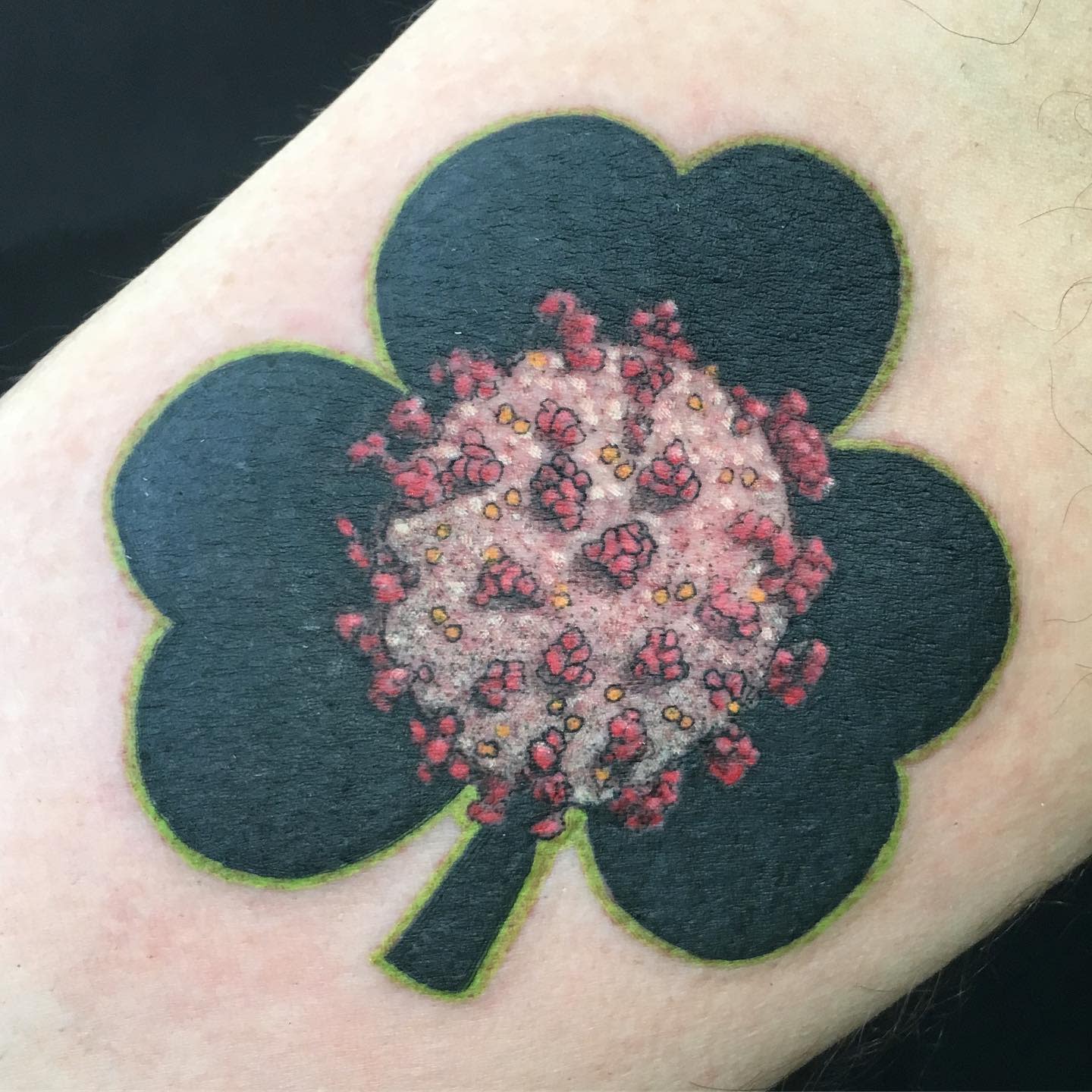 Tattoo of a shamrock with a COVID-19 virus image at its center