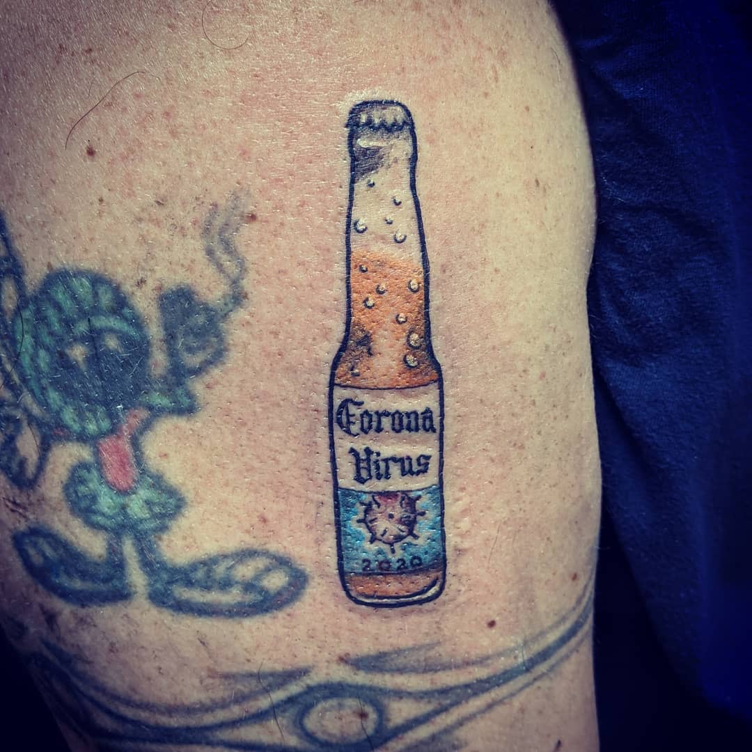 Tattoo of a beer bottle with "Corona Virus 2020" on someone's upper arm