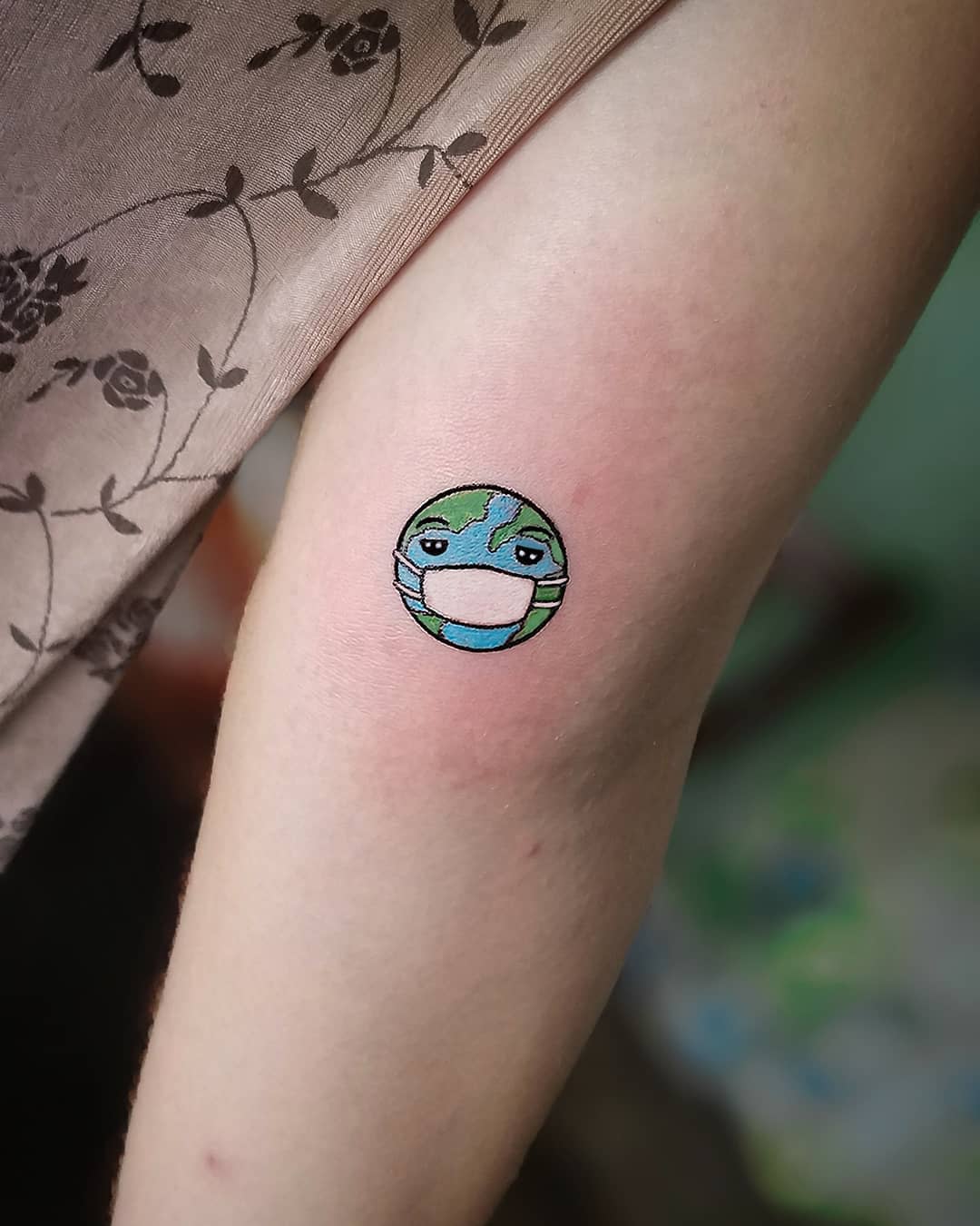 Small tattoo of an earth wearing a facemask