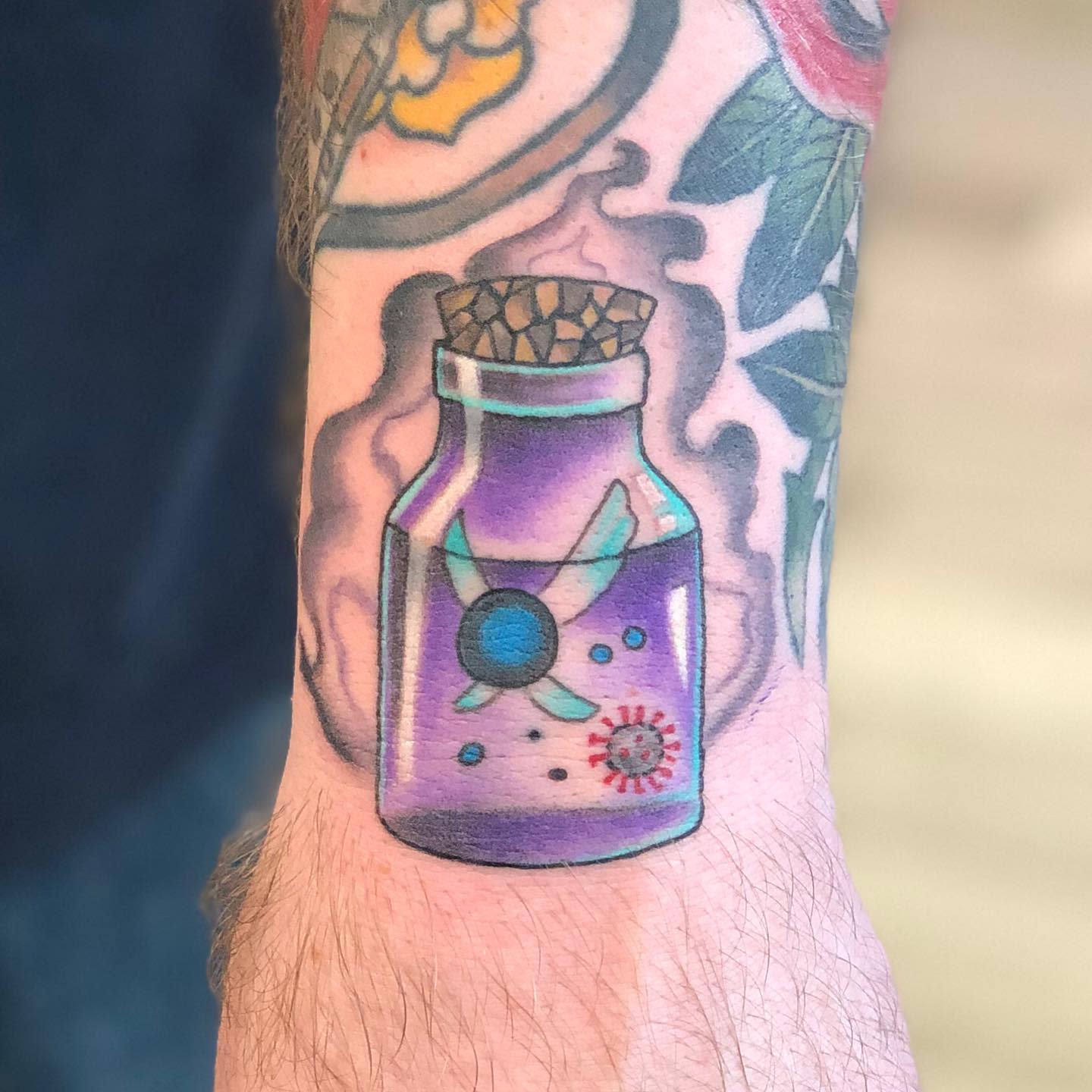 Tattoo of a purple potion bottle with a cork and virus inside it on a tattooed arm