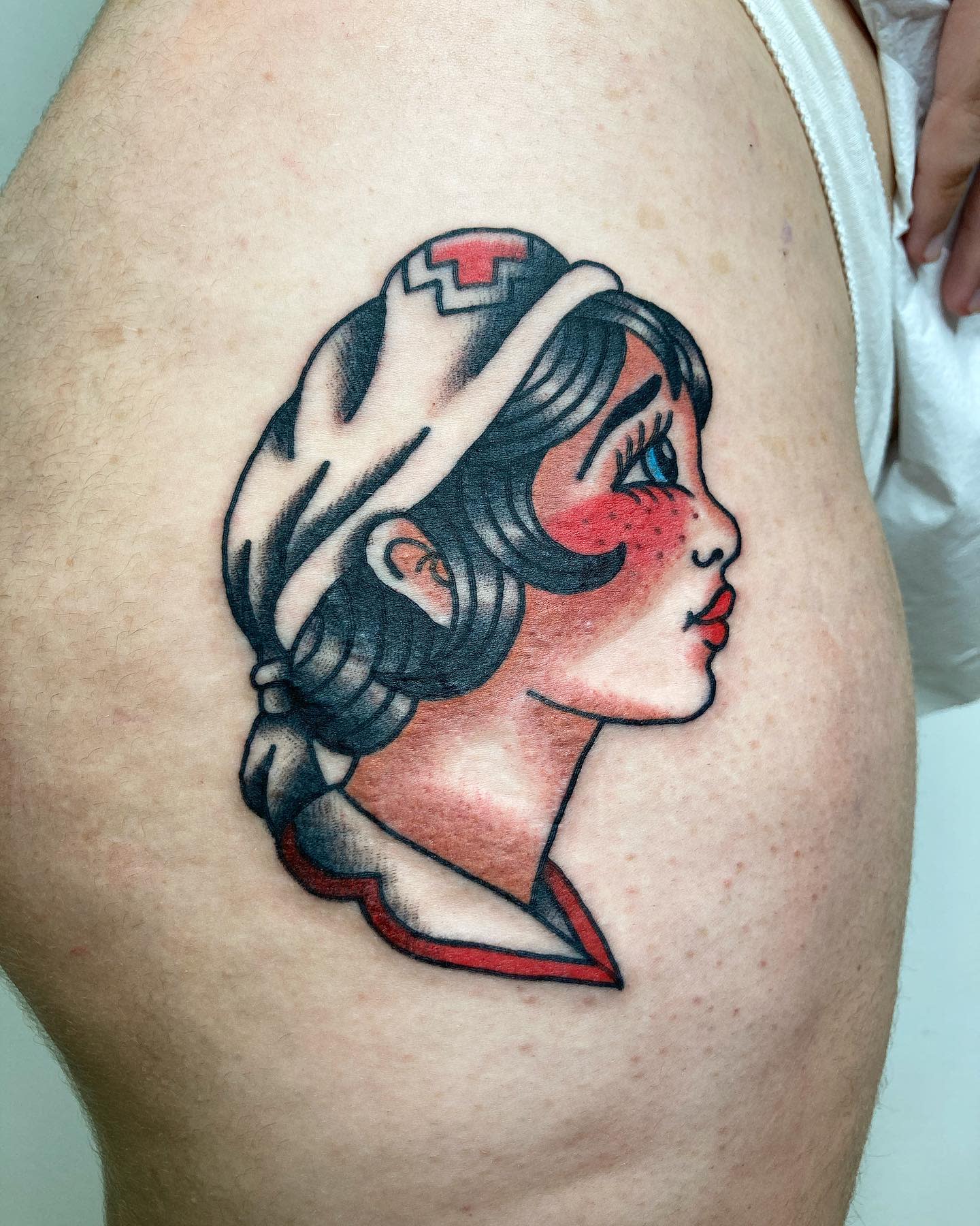 Tattoo of a nurse in old-fashioned attire on light skin, with vivid red and black colors
