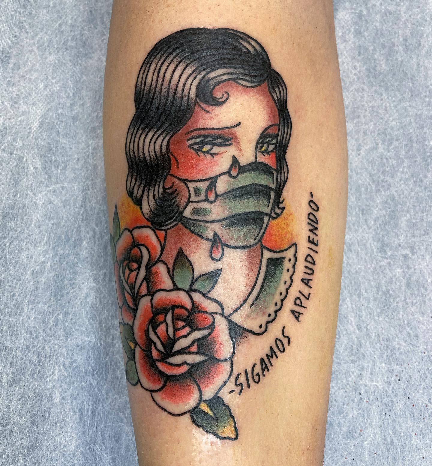 Tattoo of a woman with teardrops wearing a mask surrounded by roses with Spanish text