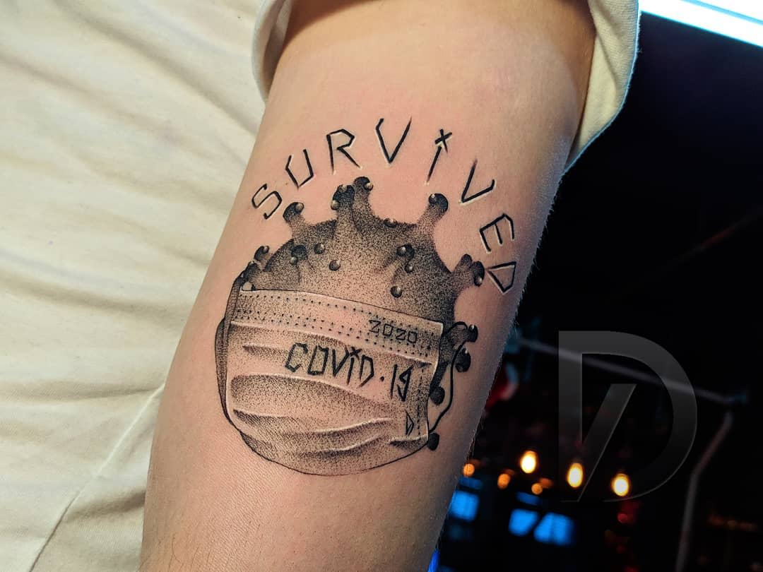 Tattoo of a virus wearing a mask with the word "SURVIVED" above it on an arm