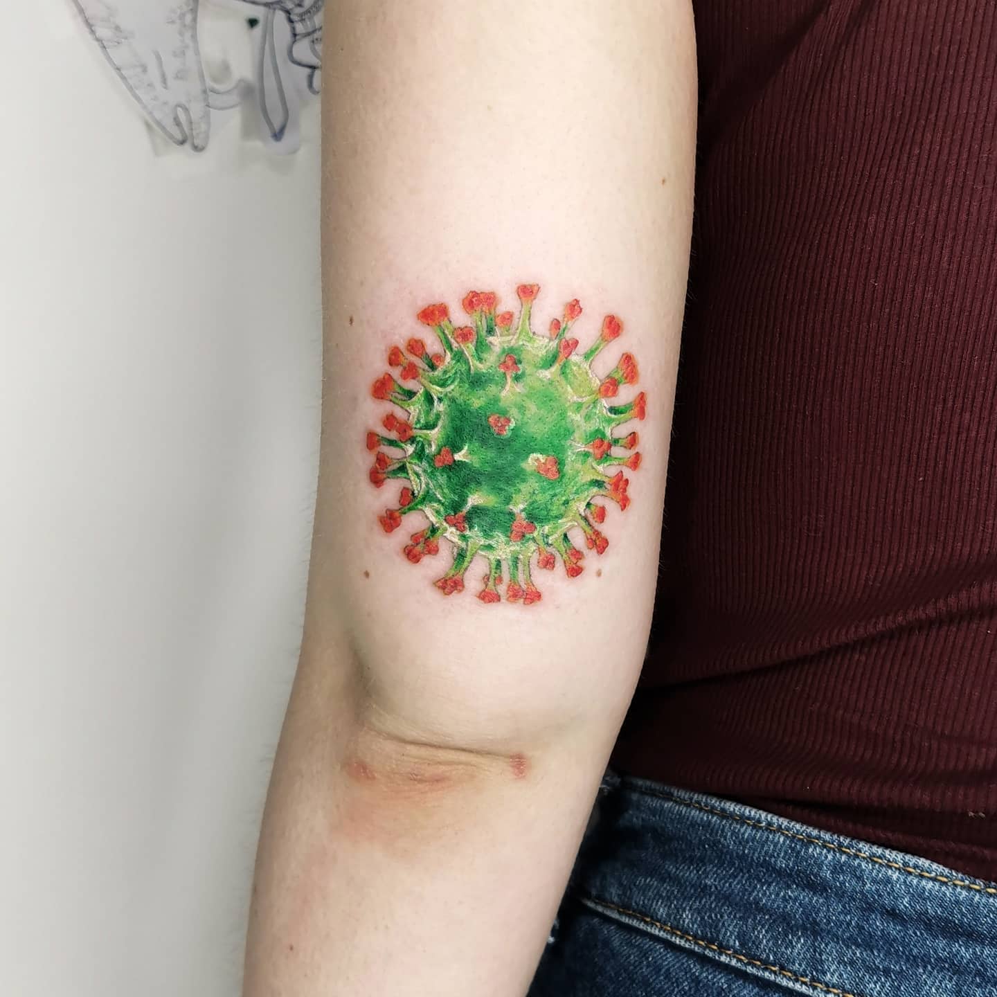 A colorful tattoo of a virus on an arm, featuring a red top and a green center design