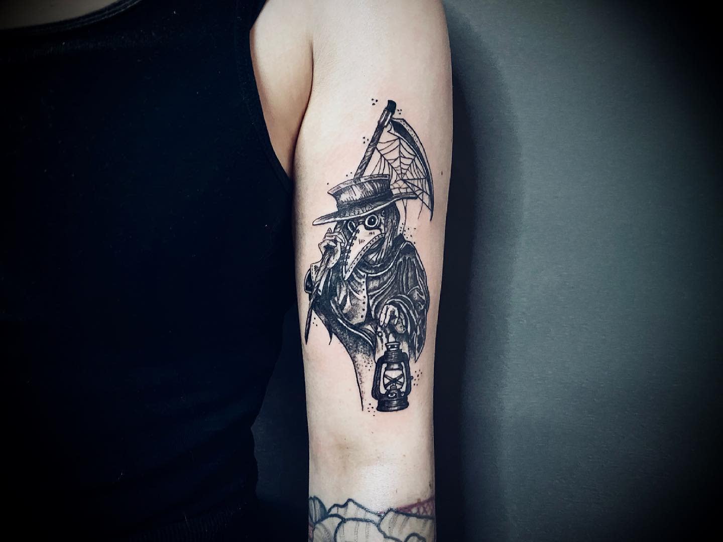 Tattoo of a plague doctor mask and cloak holding a lantern on an upper arm