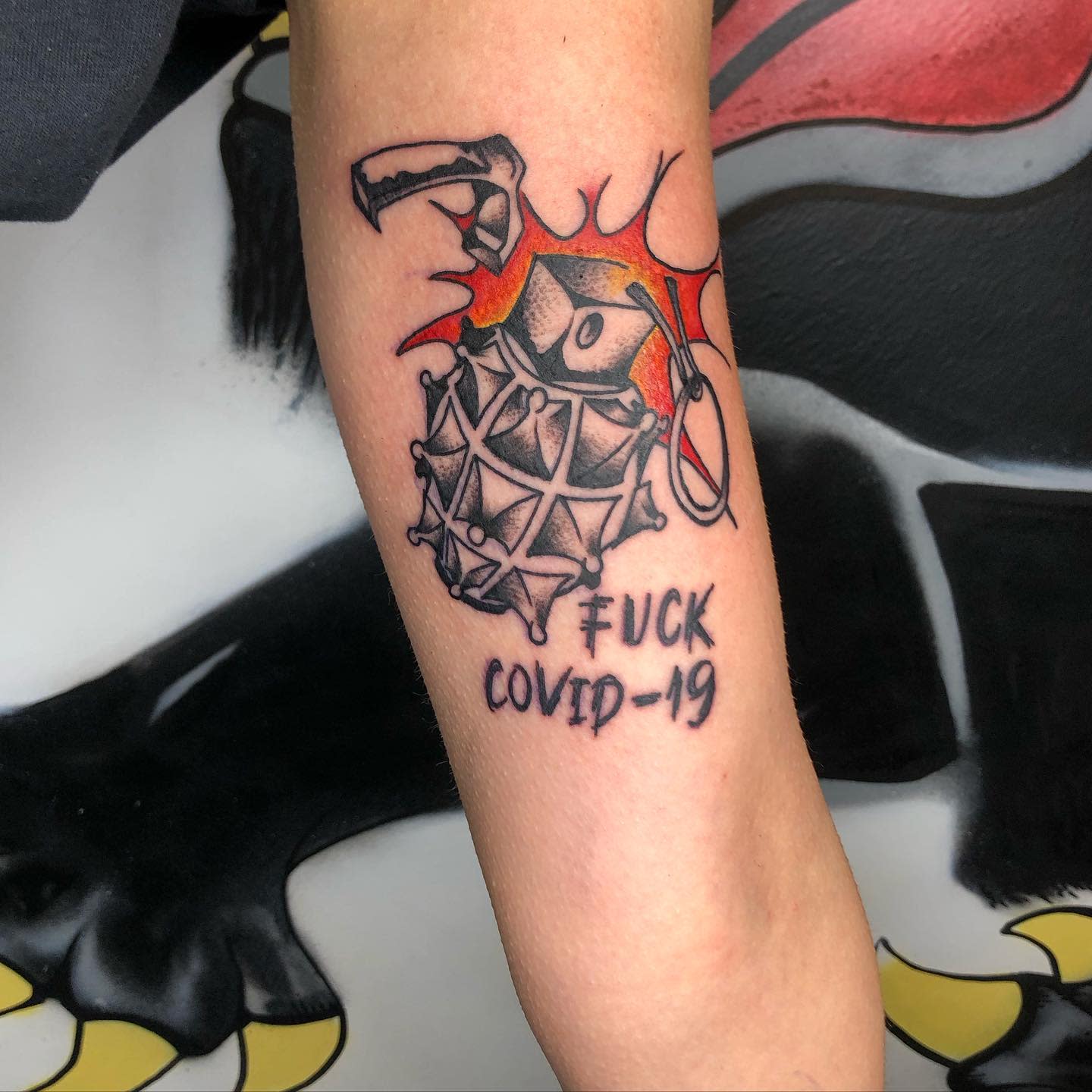 Forearm tattoo of grenade with mask, flames, and "FUCK COVID-19" text below it