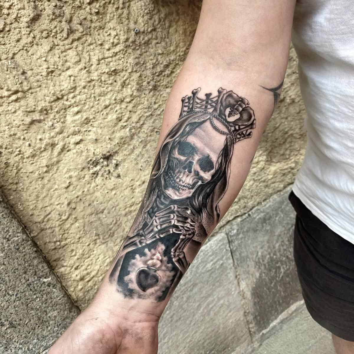 A forearm tattoo depicting Santa Muerte with a crown, holding a sacred heart in her skeletal hands