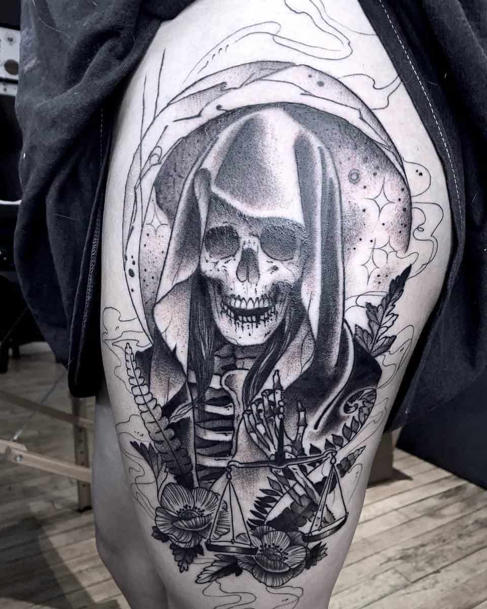 A black-and-grey tattoo of Santa Muerte holding scales, symbolizing balance and justice, with floral accents