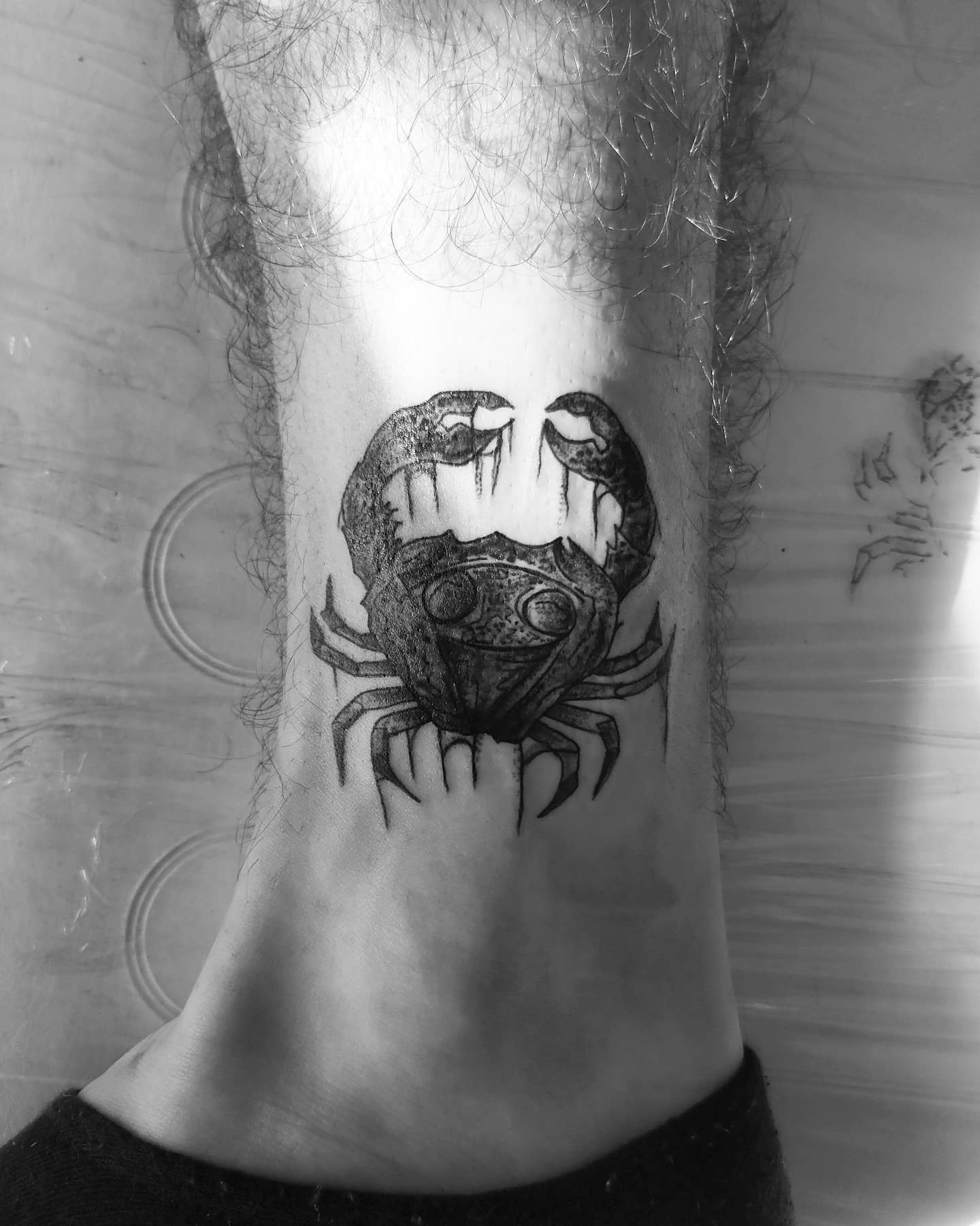 Black and white tattoo of a cancer on the inner ankle with detailed design, claws raised