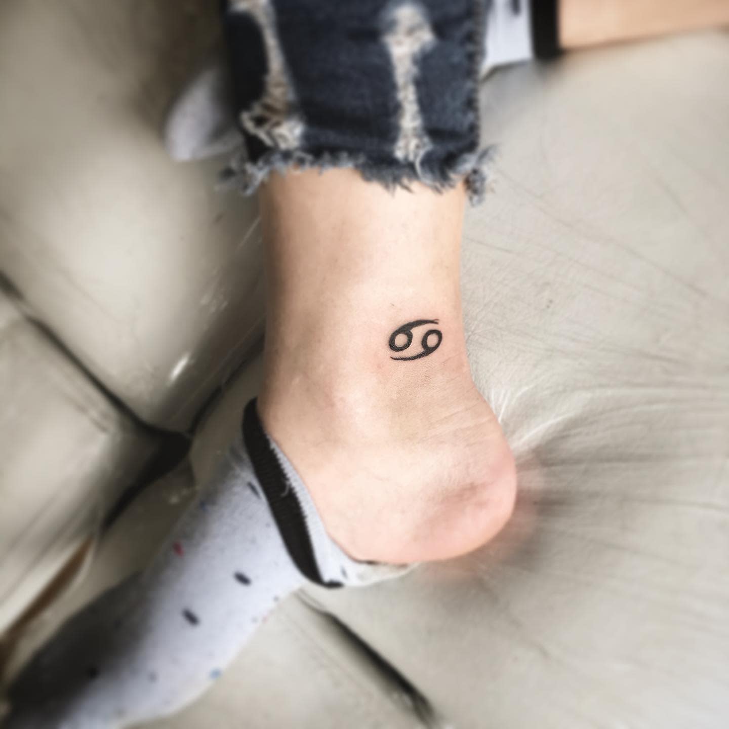 Ankle tattoo of the Cancer zodiac symbol 