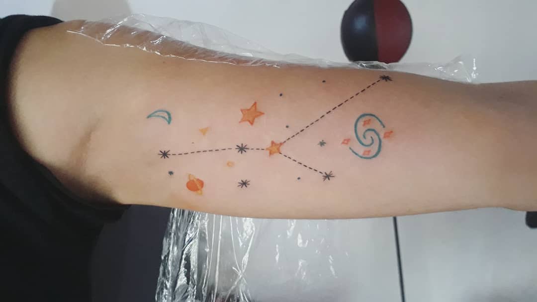 Forearm tattoo of a colorful cancer constellation with stars, crescent moon, and a swirl design