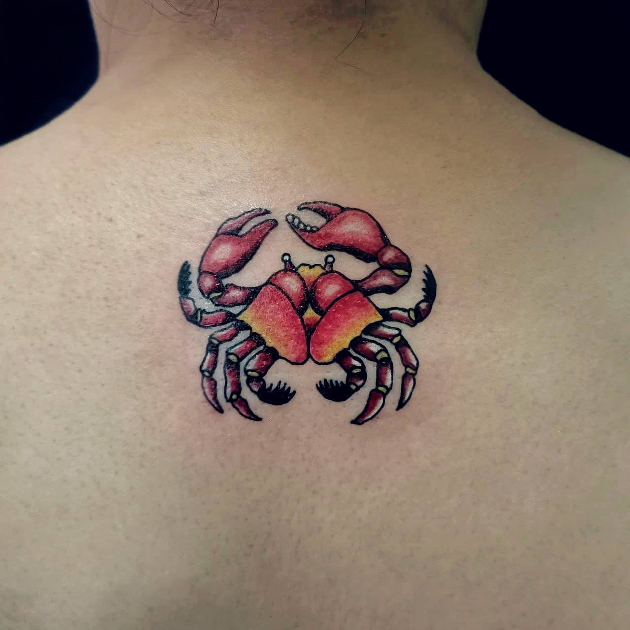 A colorful tattoo of a crab on someone's upper back