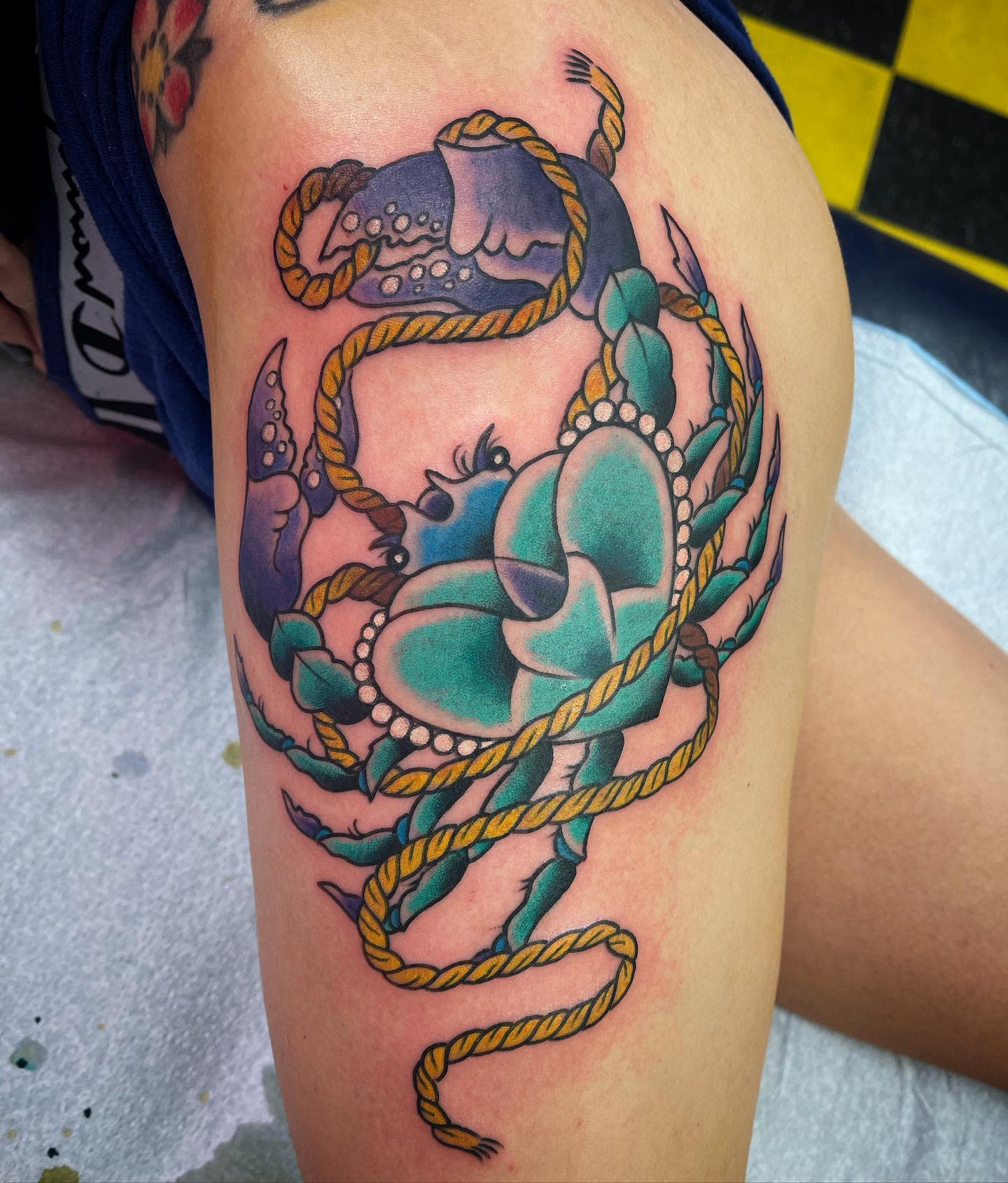 Colorful tattoo of a crab holding a heart and wrapped in a rope on an upper arm