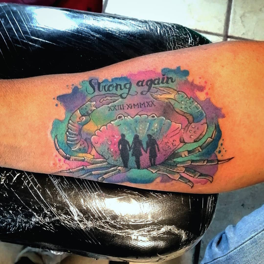Colorful cancer tattoo with "Strong again" text and silhouettes of three individuals inside it