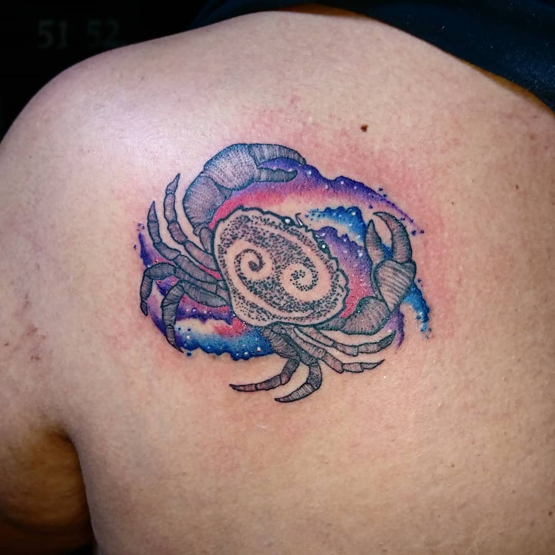 A detailed tattoo of a cancer with a galaxy background on the upper back