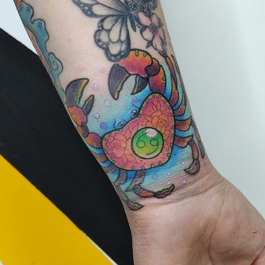 Colorful cancer tattoo with floral and zodiac sign on a forearm