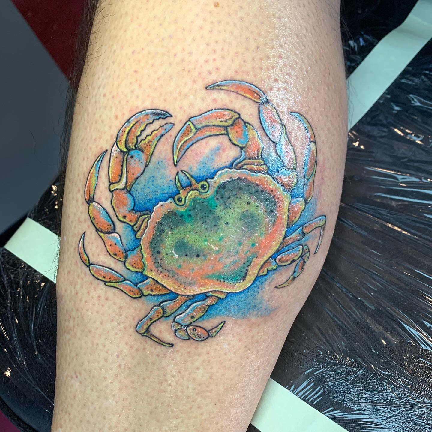 Tattoo of a colorful cancer with blue and orange details on a leg