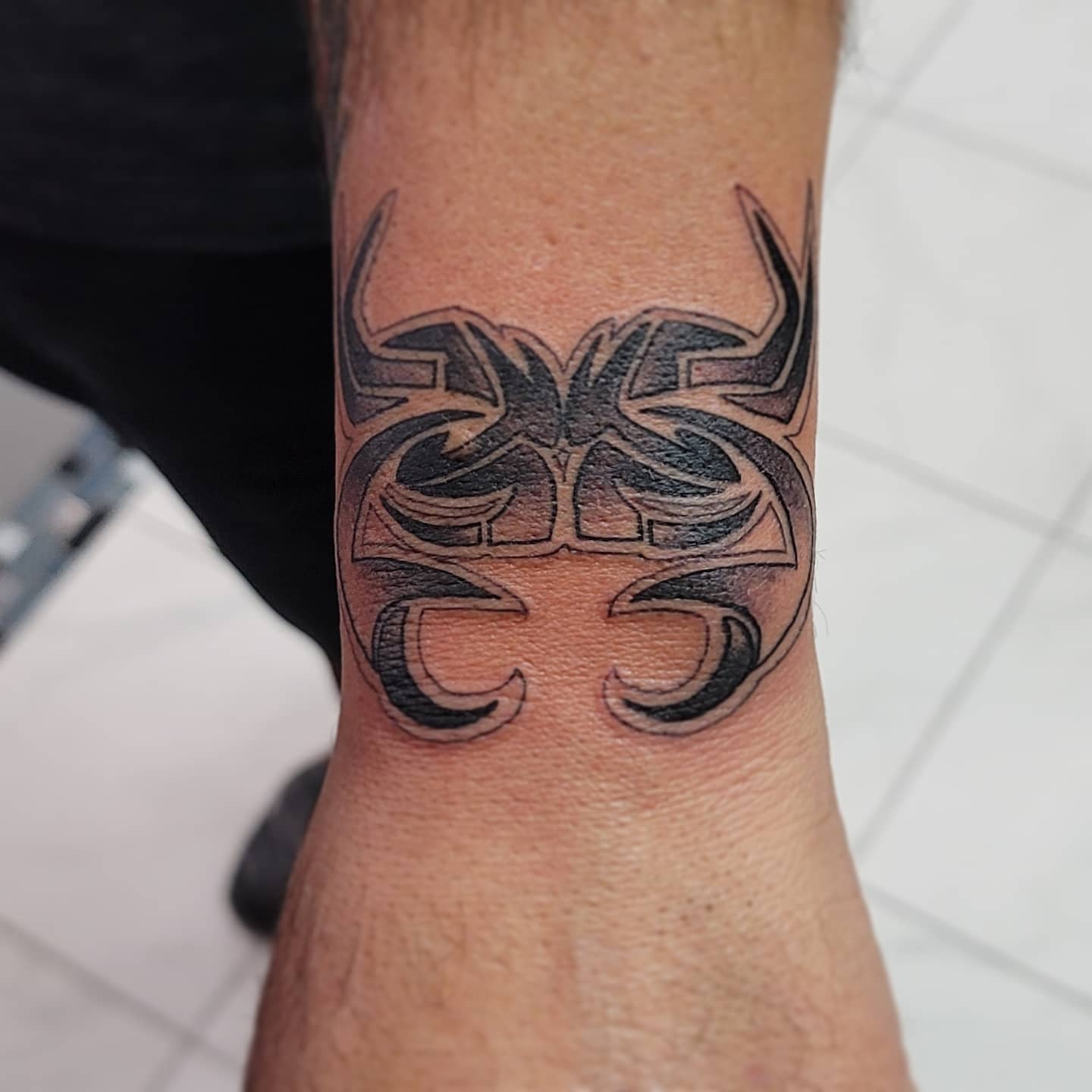 Black intricate tribal tattoo of a symmetrical cancer design on the inner wrist