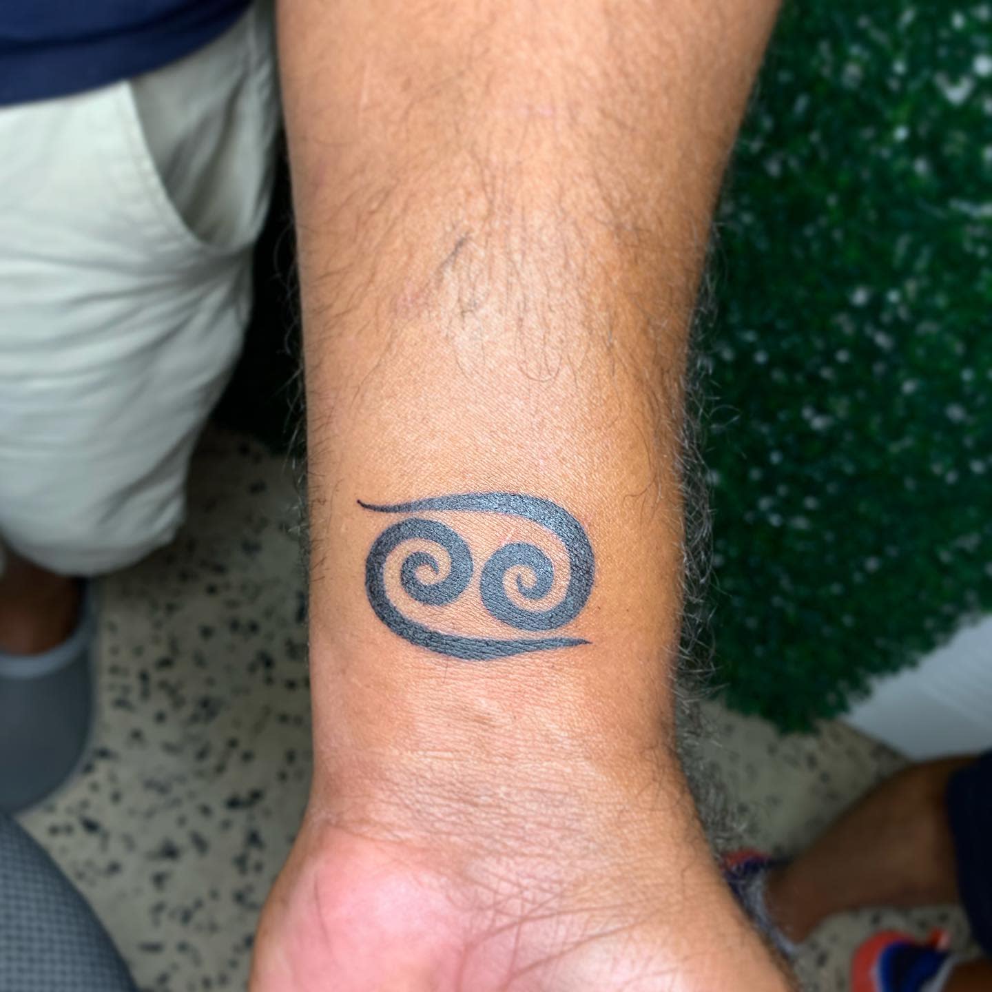 A tattoo of the Cancer zodiac sign on someone's wrist