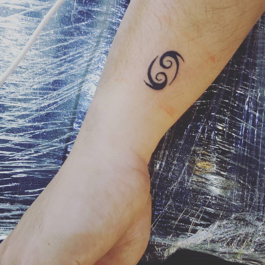 Forearm with a fresh black Cancer zodiac tattoo 