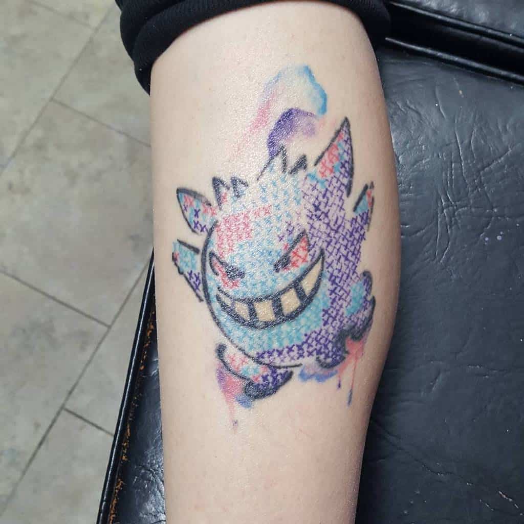 Cross-stitch style tattoo of Gengar with a watercolor effect, blending pixelated embroidery aesthetics with vibrant, ghostly colors