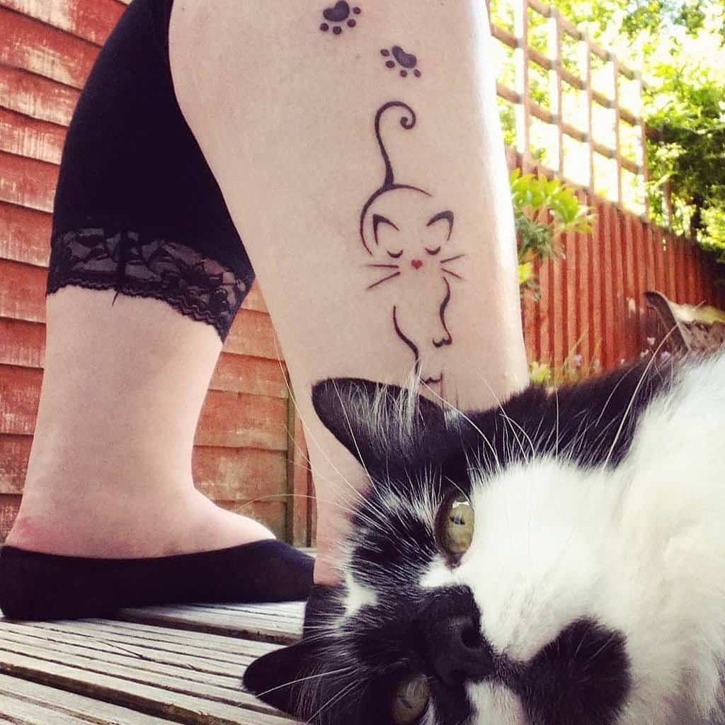 Detailed cat tattoo and paw print tattoos on a person's leg