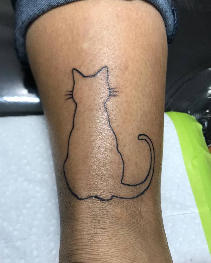 Outline tattoo of a seated feline on a leg above the ankle