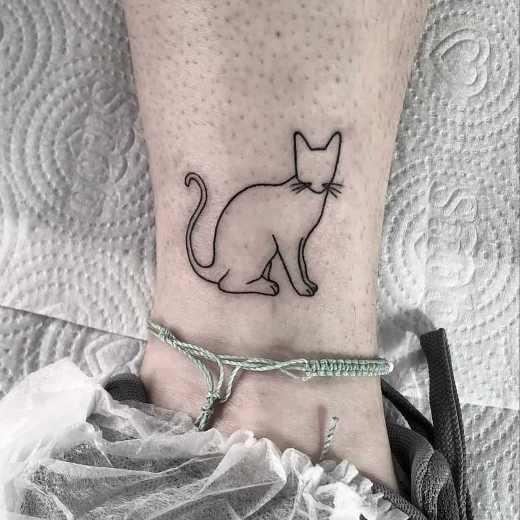 An outline tattoo of a cat on a person's ankle, complemented by a stylish green anklet above it