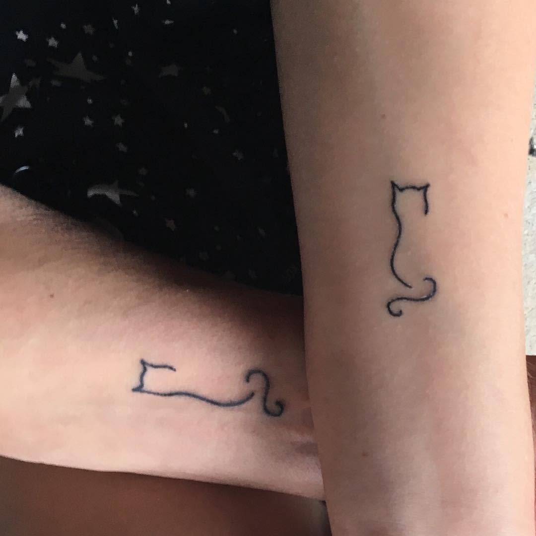 Two minimalist tattoos of cat outlines on forearm and leg, positioned symmetrically