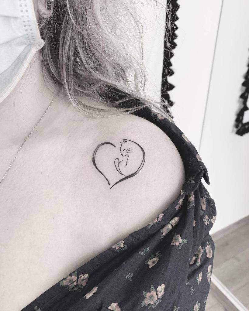 Heart-shaped cat tattoo on upper shoulder near collarbone adds a touch of feline charm