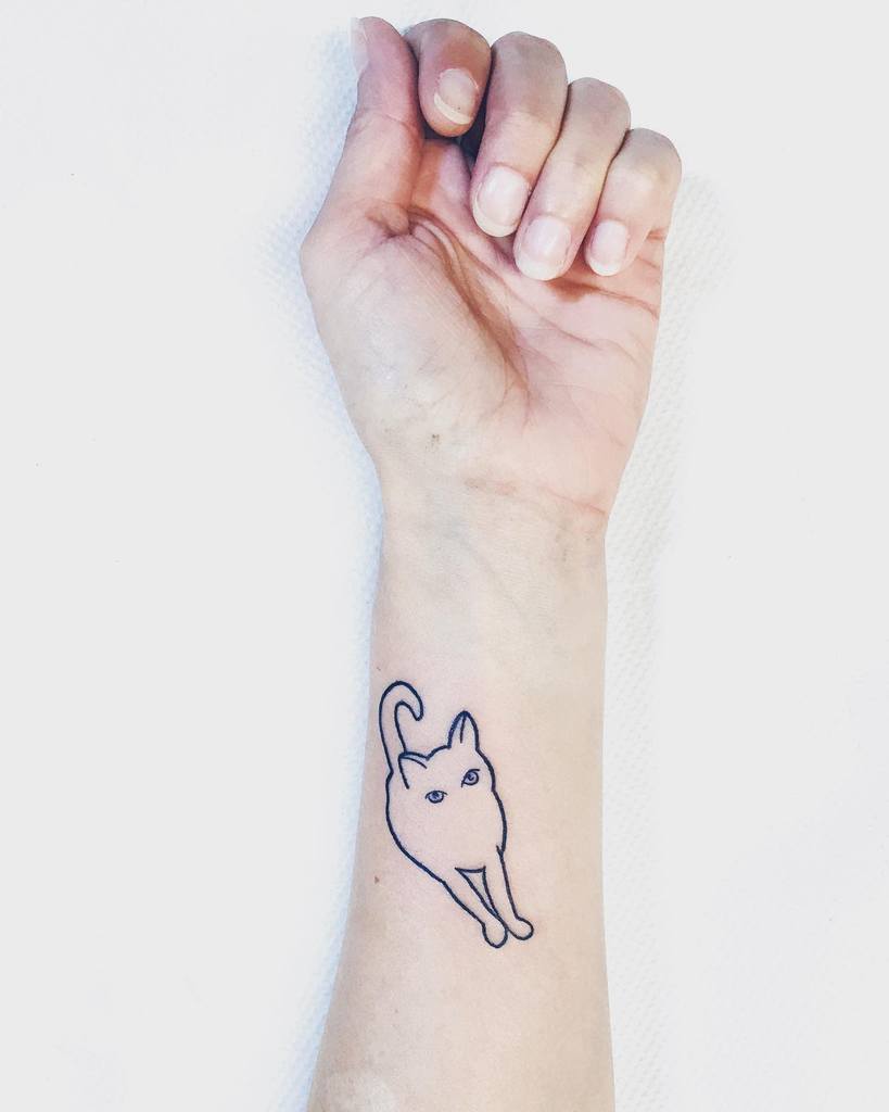 A simple outline tattoo of a cat on a person's inner wrist