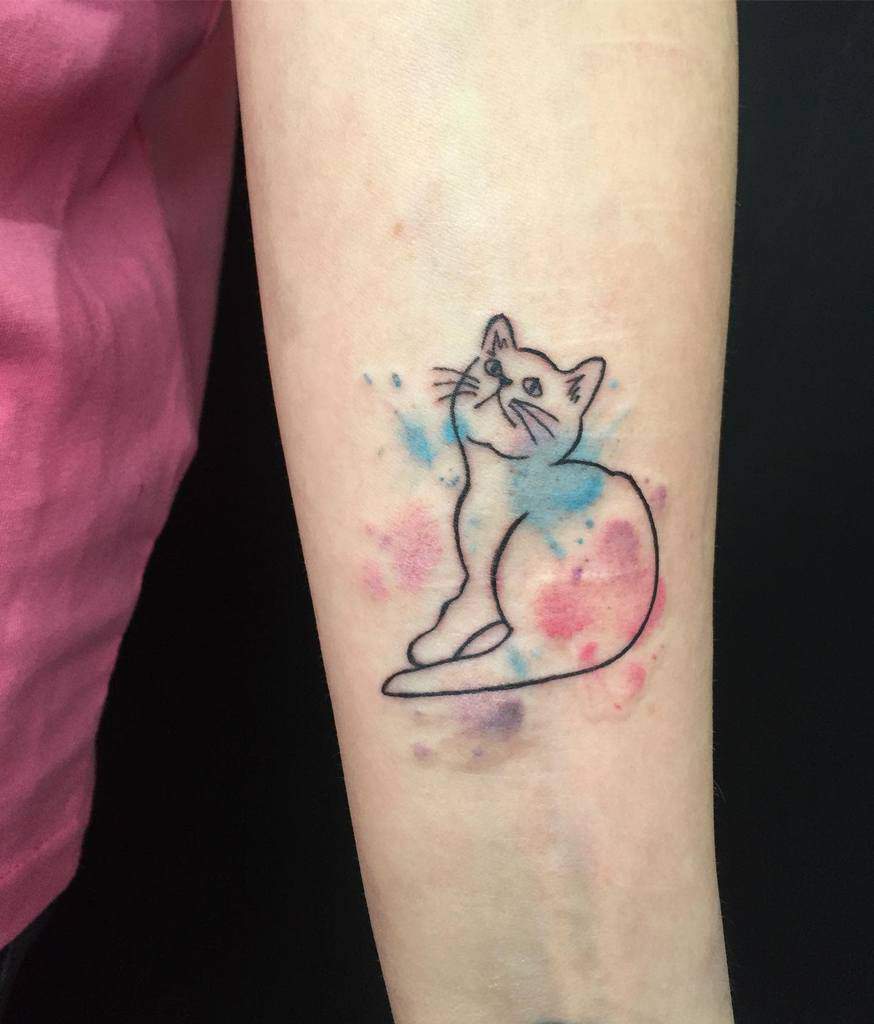 Minimalist cat tattoo with colorful watercolor splashes on an arm, elegantly peeking out from beneath a pink shirt