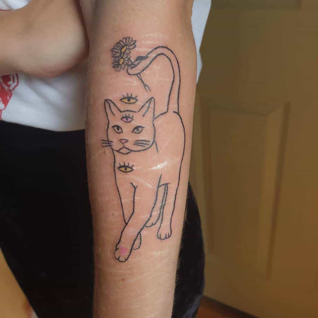 Forearm tattoo of a mystical cat with three eyes, surrounded by a daisy and two smaller eyes on the arm