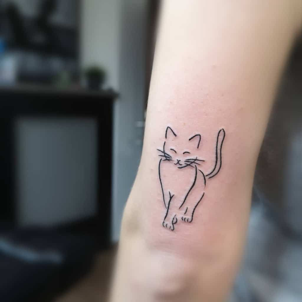 Outline tattoo of a cute, whimsical cat on an upper arm