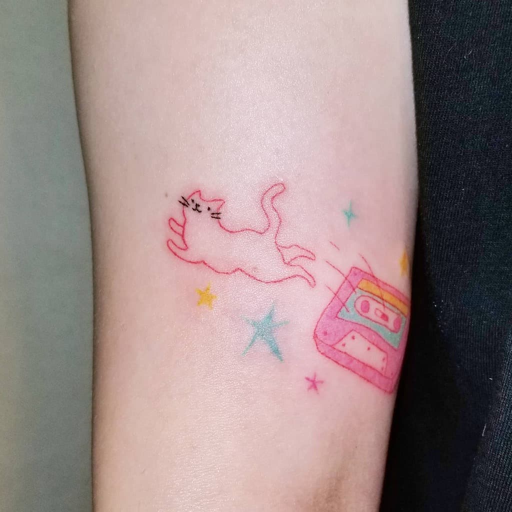 Tattoo of a cat leaping over a cassette tape with colorful stars