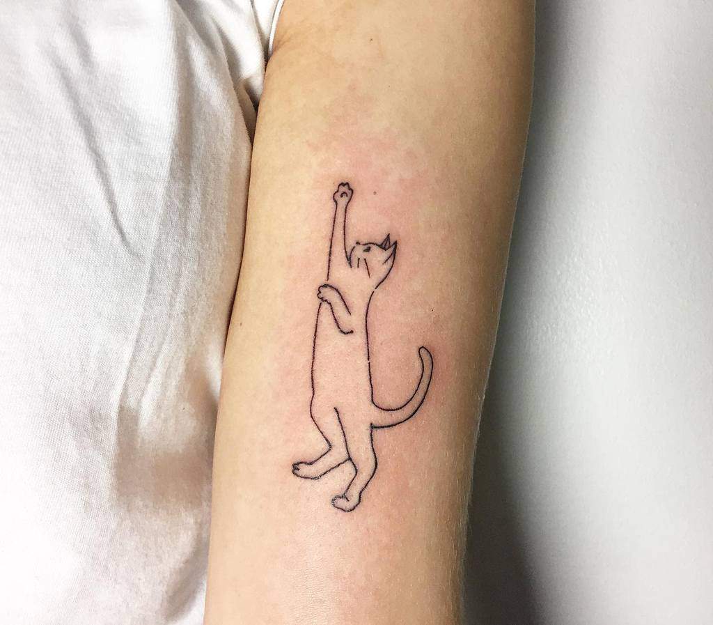 Simple cat outline tattoo on an inner arm showing a playful feline standing on hind legs reaching up