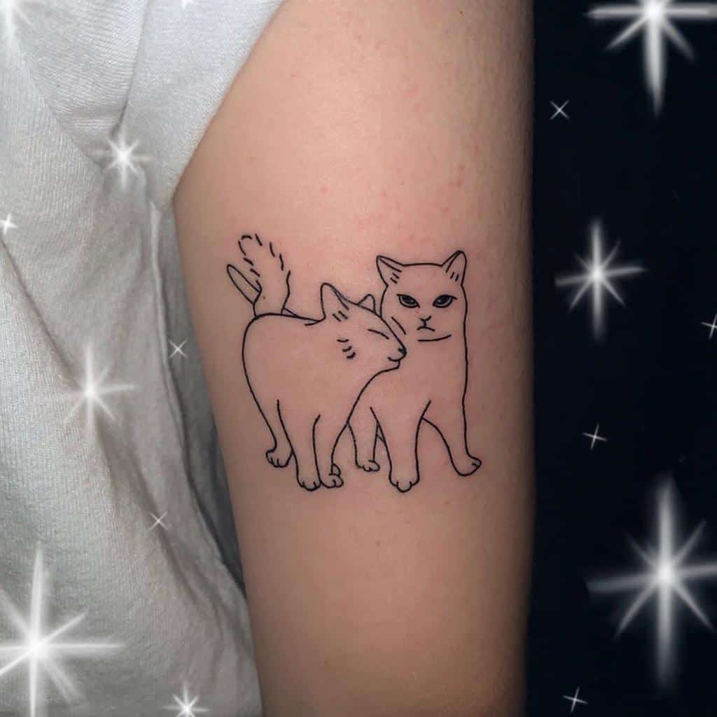 Tattoo of two outline cats, one cat nuzzling the other, on a person's upper arm