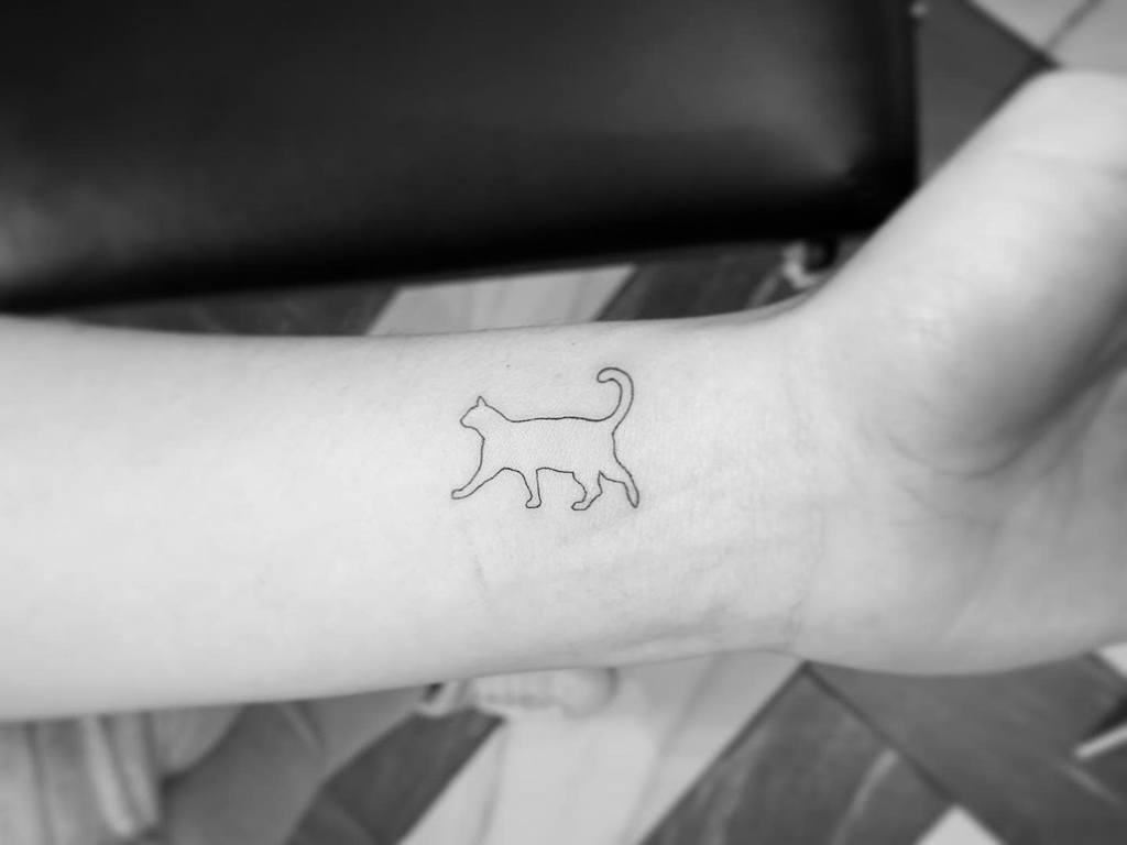 Outline tattoo of a walking cat on a wrist