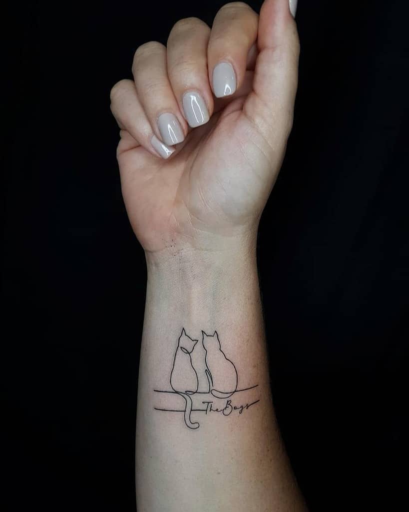 Wrist tattoo of two outlined cats sitting side by side on a branch