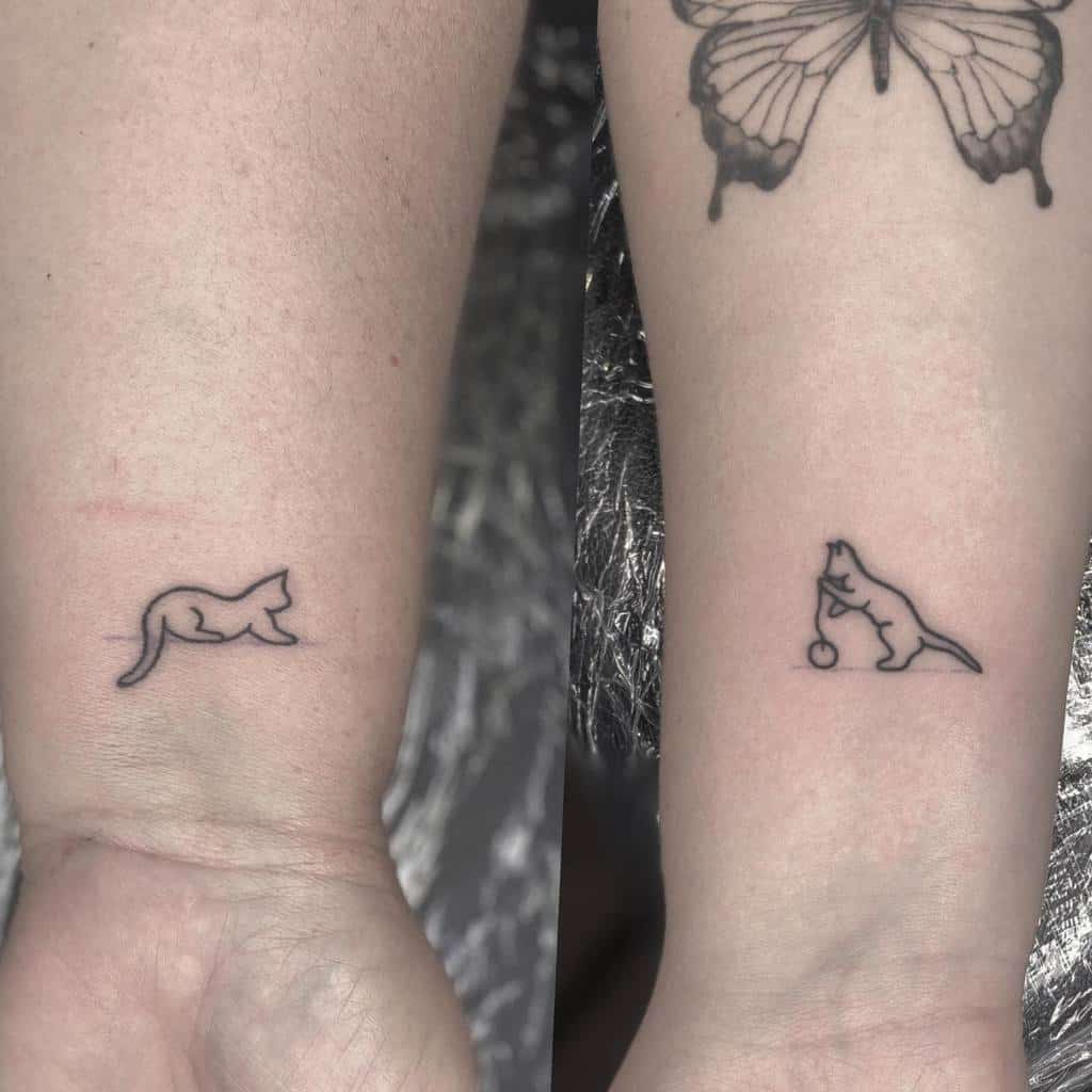 Two simple black cat tattoos, one lying down and the other playing with a ball of yarn, adorn the wrist