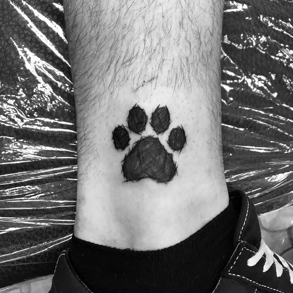 A black cat paw print tattoo graces the back of a person's ankle