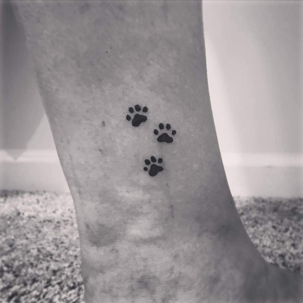 Black and white image of three cat paw print tattoos on a person's leg