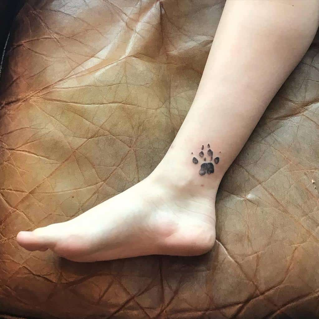 A cat paw print tattoo is on the inside of the lower leg above the ankle