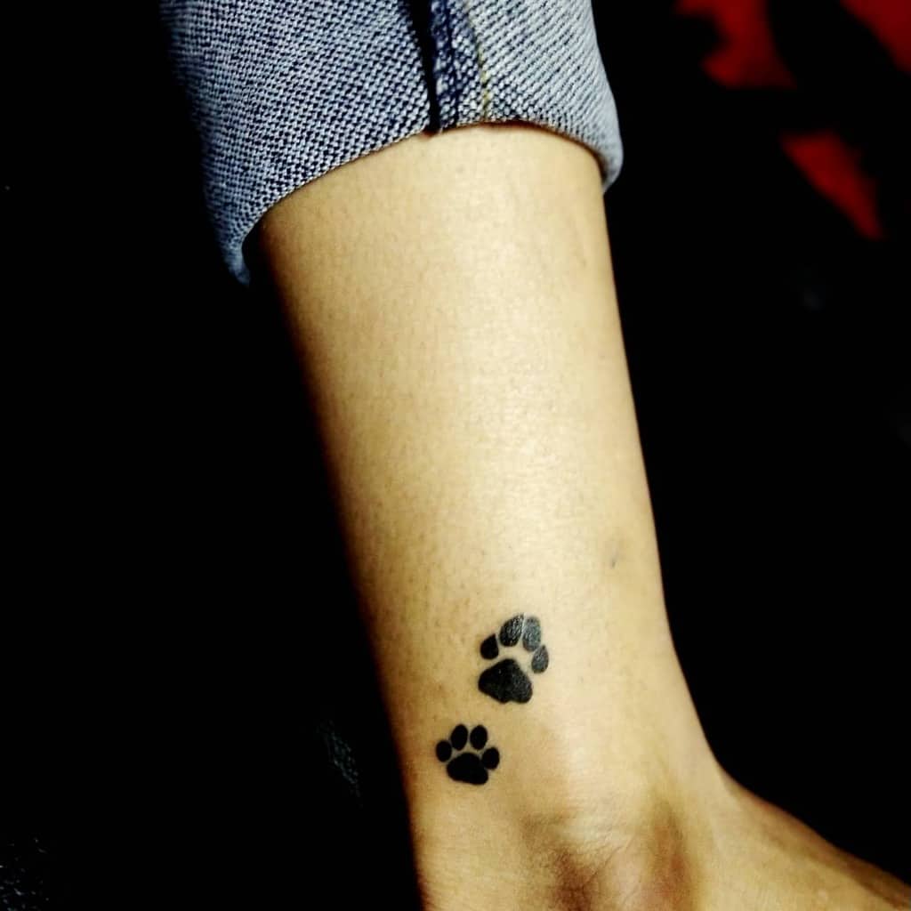 Tattoo of two black cat paw prints on a person's ankle