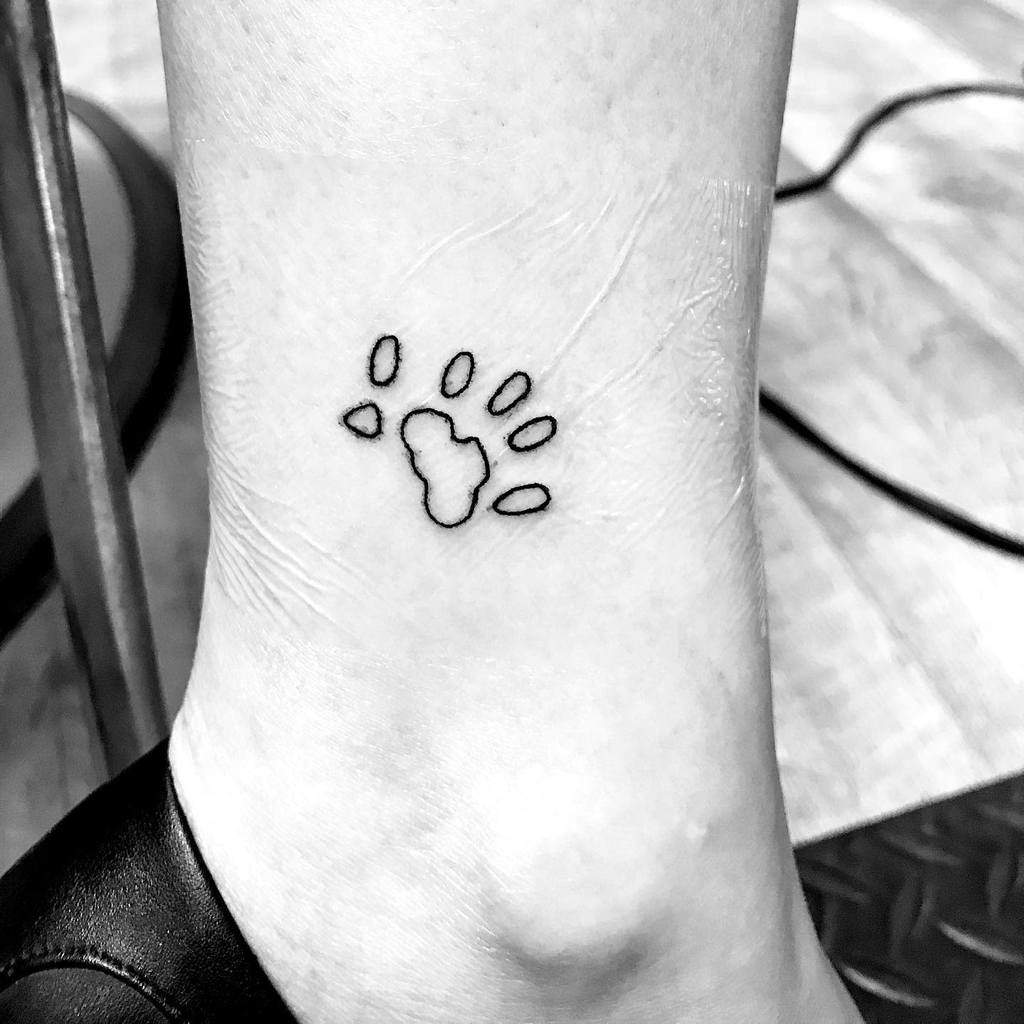Black outline tattoo of a cat paw print on an ankle