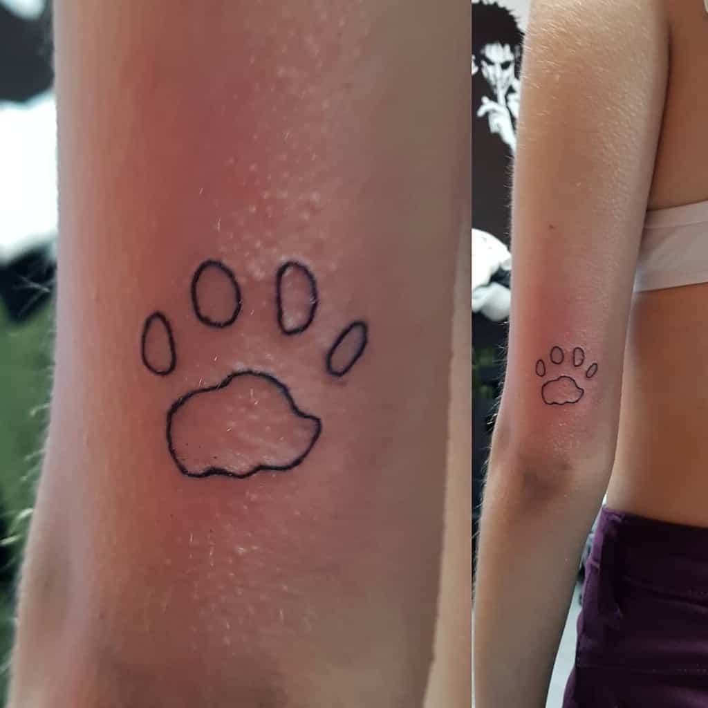 A black outline tattoo of a cat paw print on a forearm