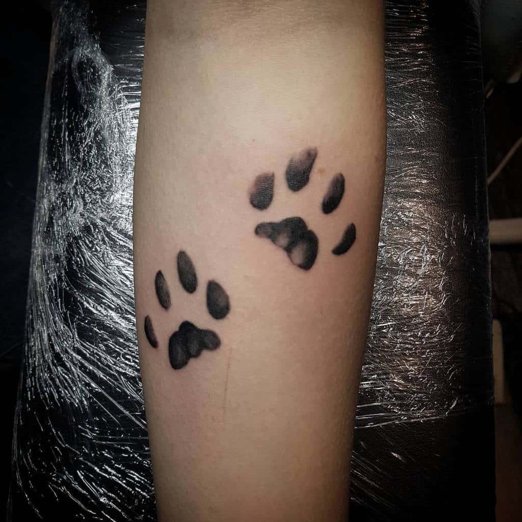 Tattoo of two black cat paw prints on an inner forearm