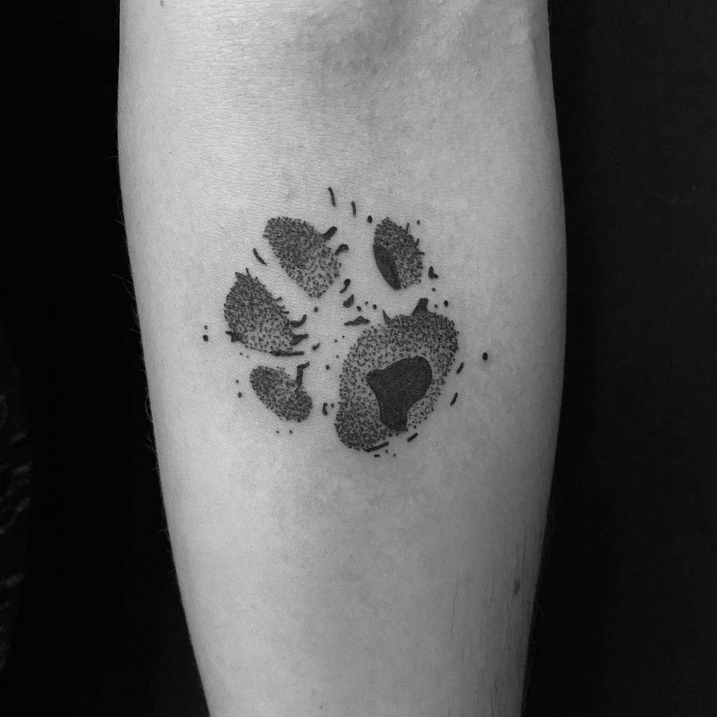 A black and white tattoo of a cat paw print elegantly inked on a person's forearm