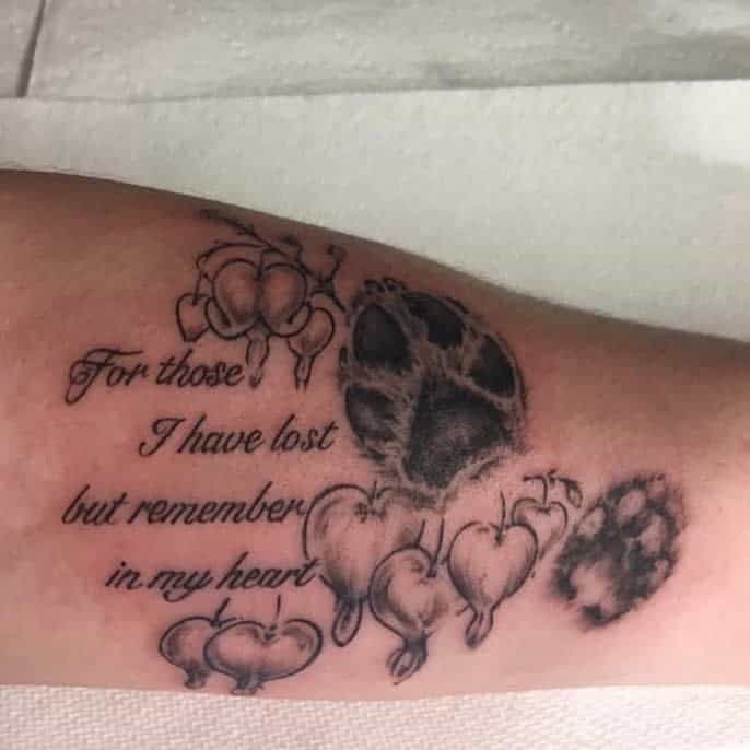 Tattoo featuring text, cat paw prints, and heart flowers on an arm